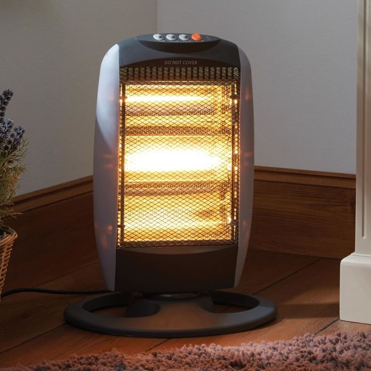 an electric heater sitting on top of a wooden floor next to a vase with flowers