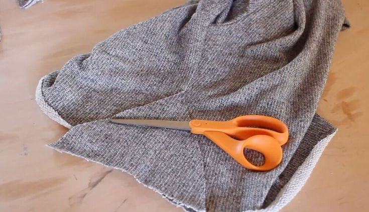 an orange pair of scissors sitting on top of a piece of gray fabric next to a pair of scissors