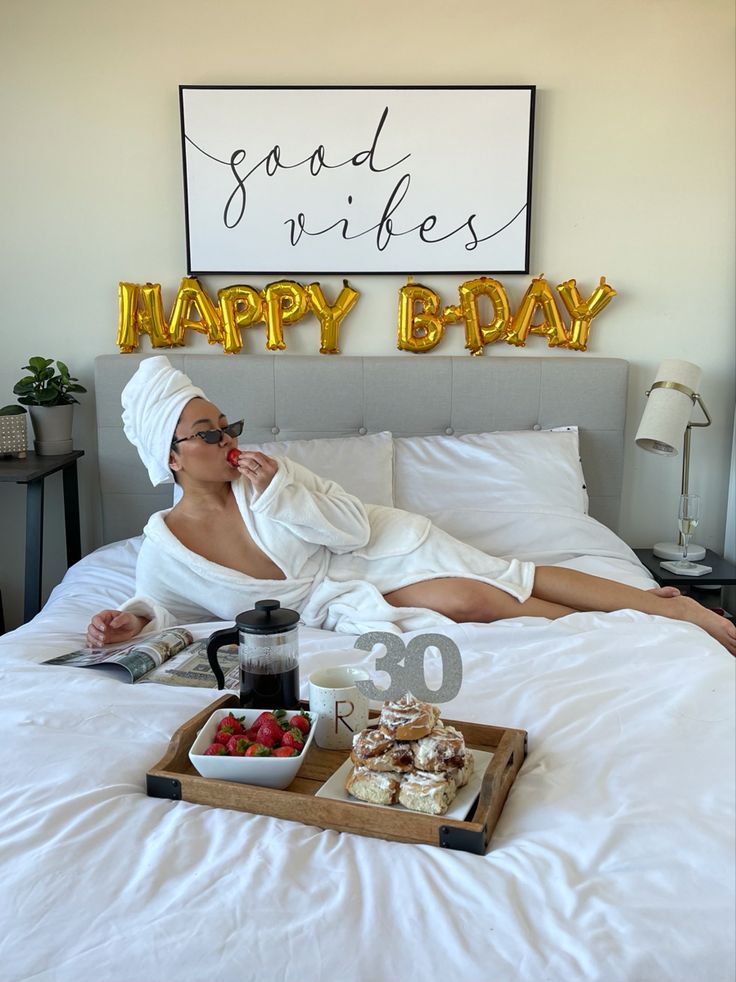 a woman laying in bed with food and drinks on the trays next to her