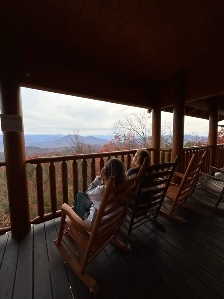 two people sitting on rocking chairs looking out at the mountains in the distance from an outdoor porch