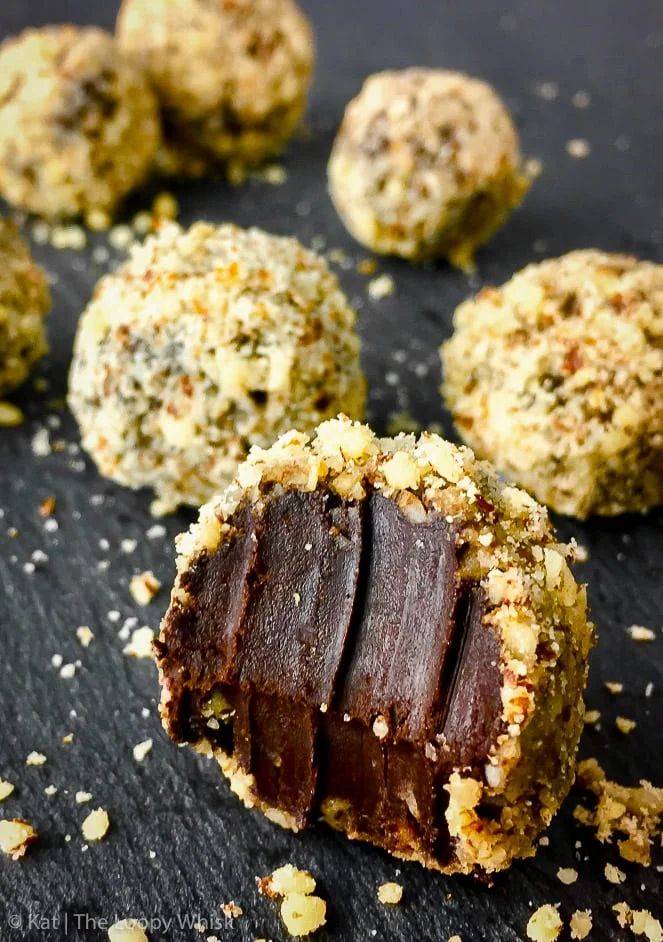 chocolate and coconut balls on a black surface with nuts scattered around them, ready to be eaten