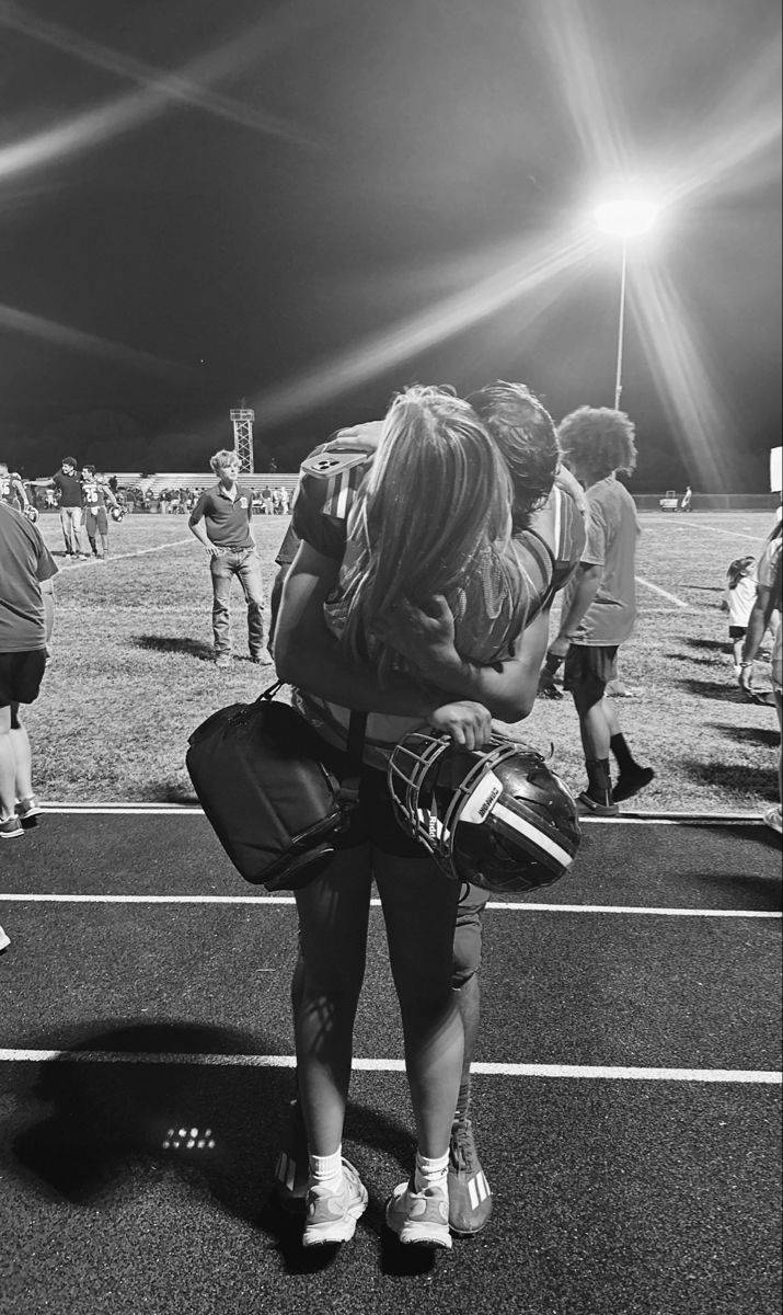 black and white photograph of two girls hugging each other on a football field at night