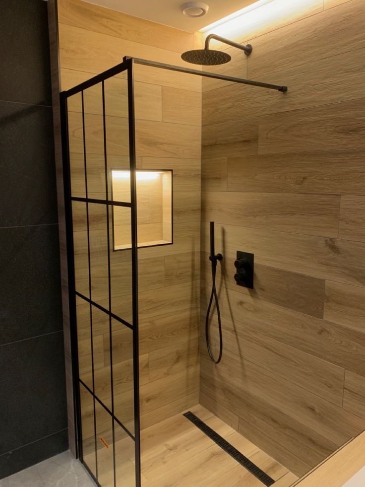 a bathroom with wooden walls and flooring has a glass shower stall, black faucet, and wood paneled wall