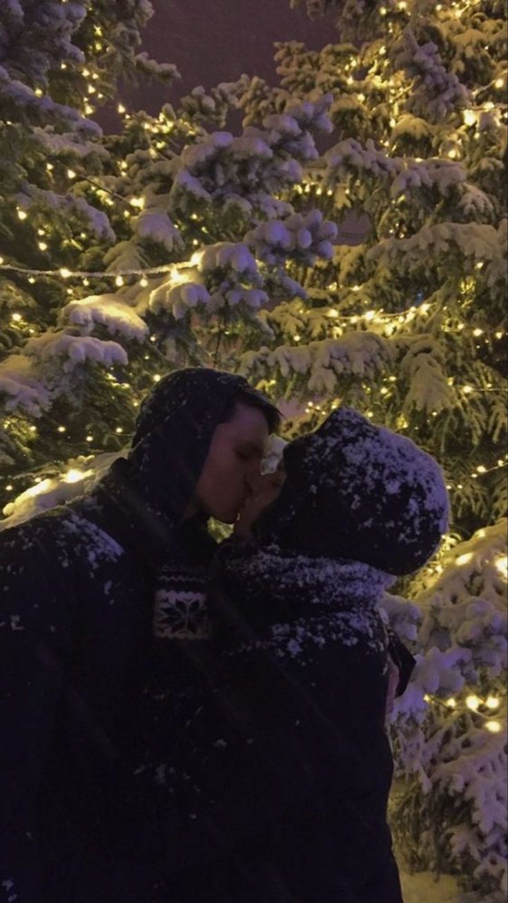 a man standing in front of a christmas tree covered in snow with lights behind him