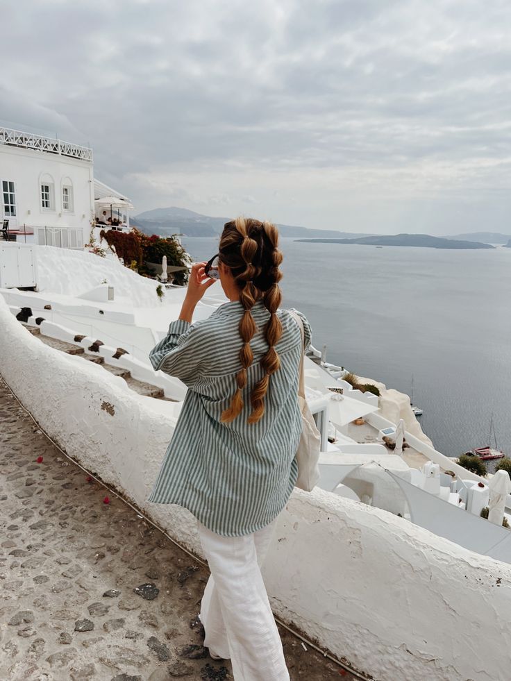 a woman standing on top of a white building next to the ocean