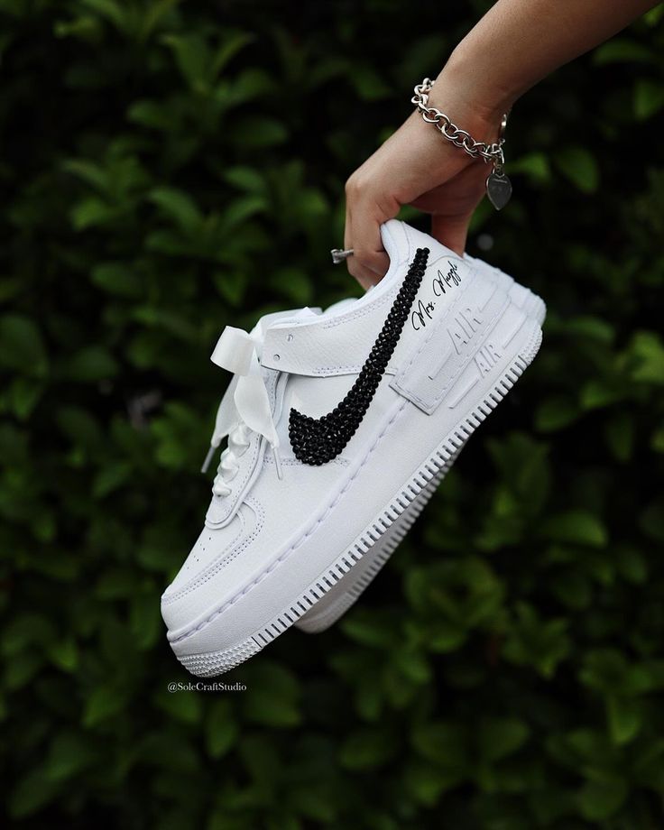 a person is holding up a white nike air force shoe with black swarong on the side