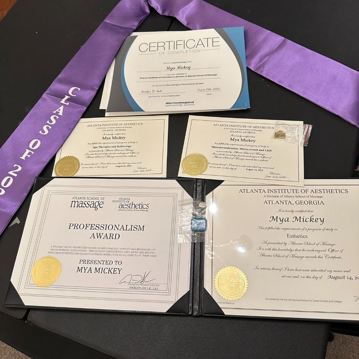 three diplomas and two certificates on a table with purple ribbon around them,