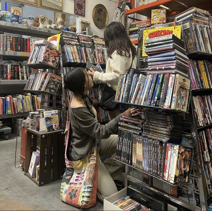 two women are looking at cds in a store aisle with shelves full of dvds and movies