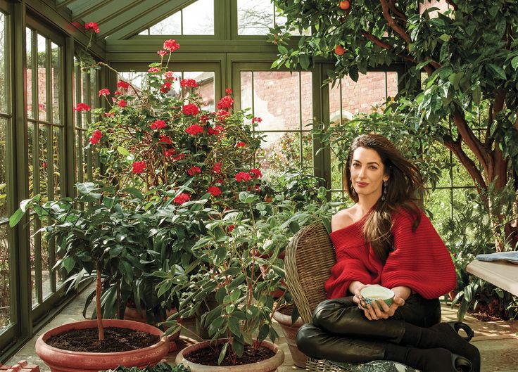 a woman sitting on a chair in a greenhouse with potted plants and flowers around her