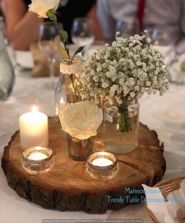 flowers and candles are sitting in vases on a wooden slice at a table with people