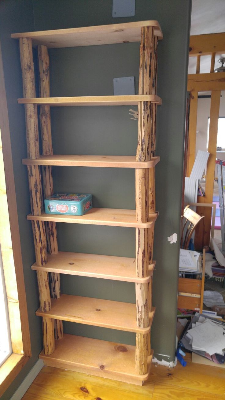 a book shelf made out of logs in the corner of a room with wood flooring