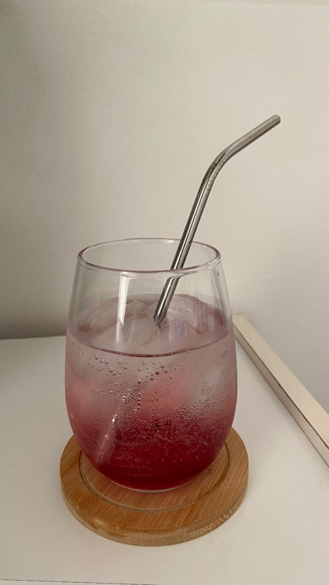 a drink in a wine glass with a straw sticking out of the top, on a wooden coaster