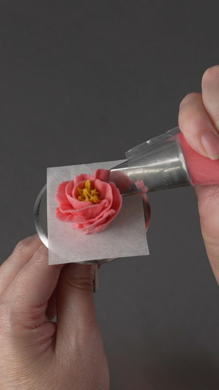 a person holding a piece of paper with a pink flower on it and a silver object in the other hand