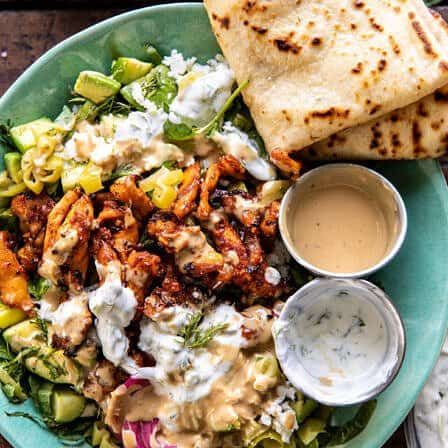 a salad with chicken, lettuce and dressing on a plate next to pita bread