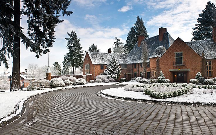 a brick driveway surrounded by snow covered trees and bushes in front of a large red brick house