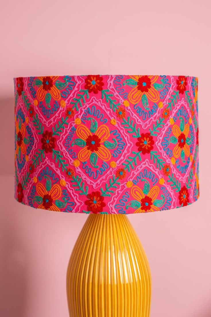 a yellow vase with a pink and blue lamp on it next to a pink wall