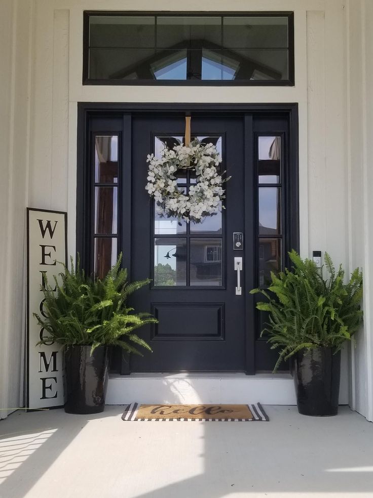 two potted plants are sitting on the front porch next to a black door and welcome sign