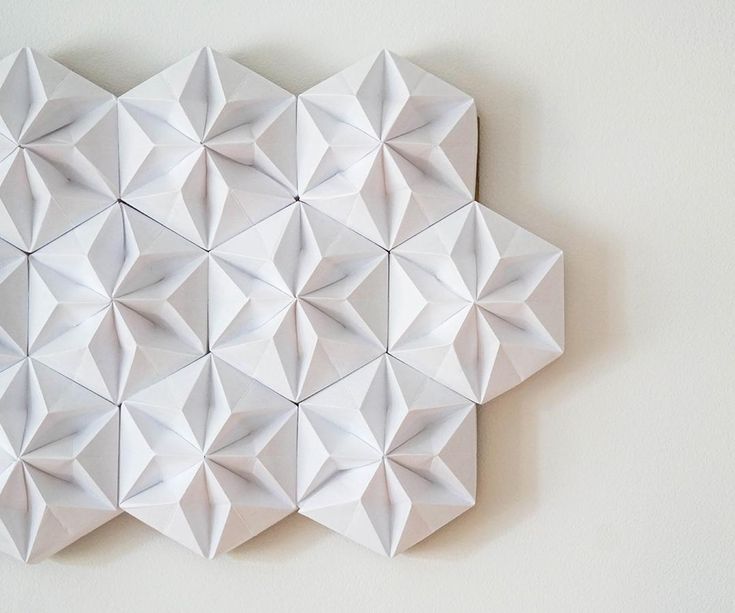 an origami wall hanging on the wall with white paper folded in hexagonal shapes