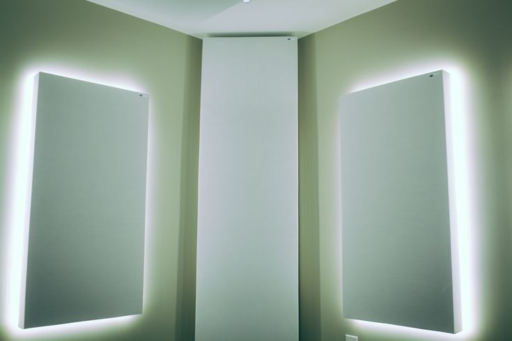 two mirrors with lights on each side of them in a white room next to a wall