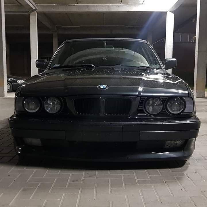 the front end of a black bmw car parked in a parking garage with its lights on