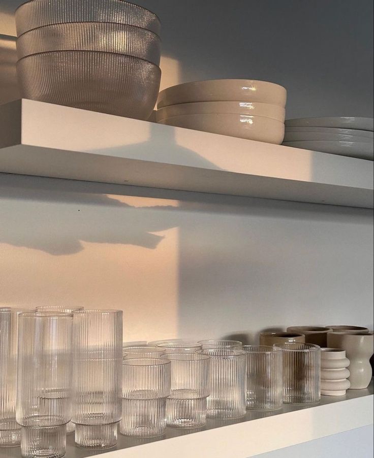 many empty glasses are sitting on the shelf in front of plates and bowls that have been placed on them