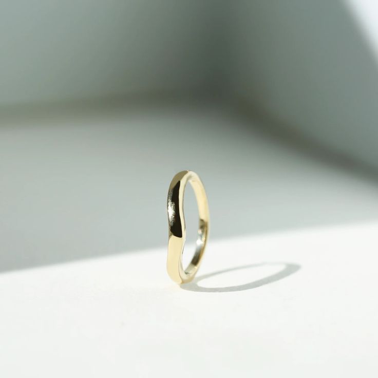 a yellow gold wedding ring on a white surface with shadows from the light coming in