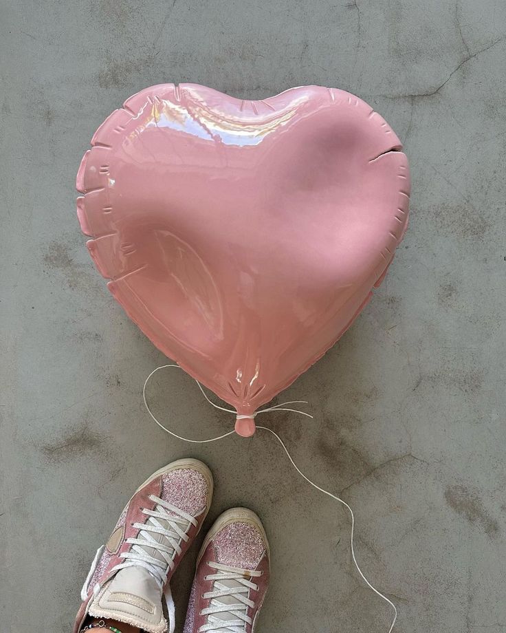 a pink heart shaped balloon sitting next to a pair of sneakers