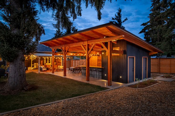 a backyard with a covered patio and outdoor dining area in the evening time, lit up by string lights