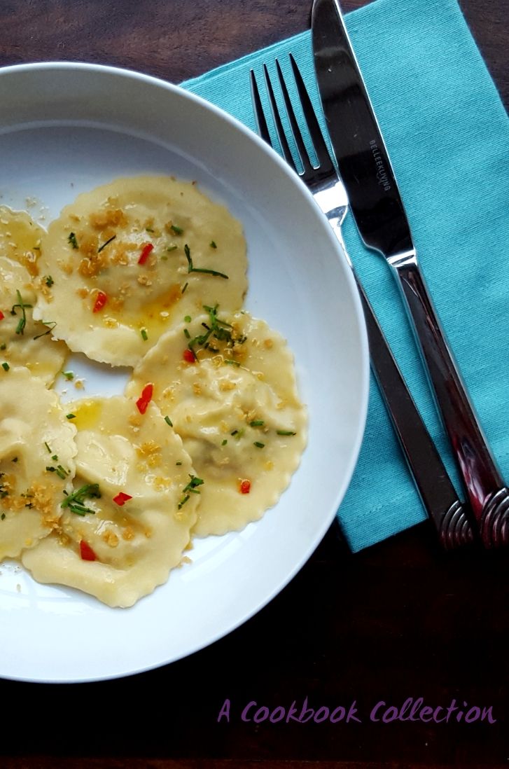 three ravioli on a white plate with silverware next to it and a blue napkin