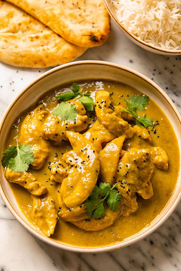 a bowl filled with chicken curry next to some pita bread on a marble surface