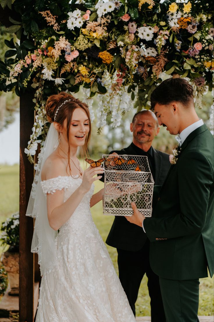 a bride and groom exchanging vows under an outdoor floral covered chute at their wedding