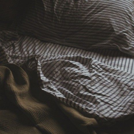 an unmade bed with striped sheets and pillows