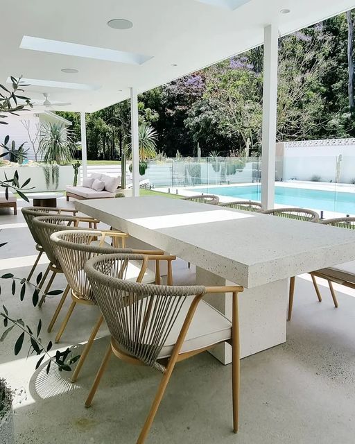 an outdoor dining area with chairs, table and pool in the backround behind it