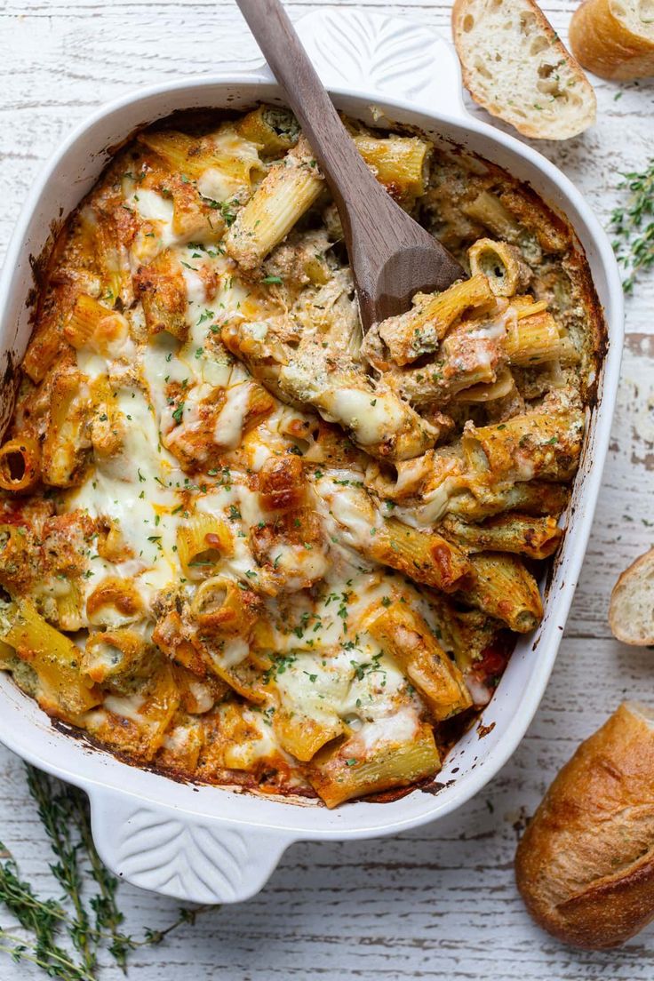 a casserole dish with chicken, artichokes and bread on the side