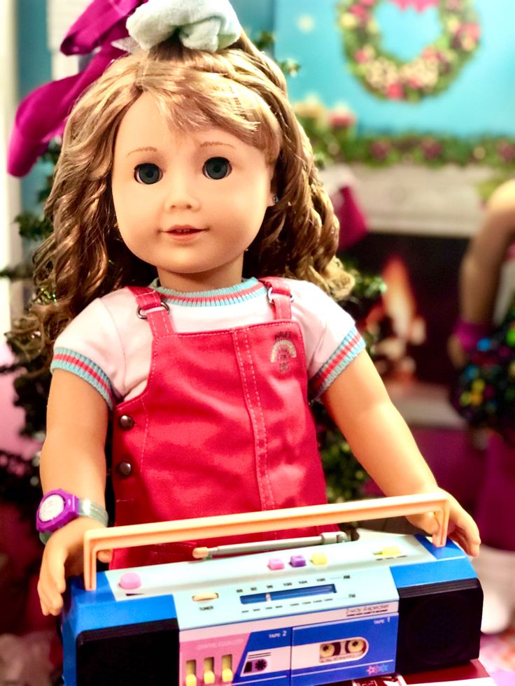 a doll is holding a radio in front of a christmas tree with presents on it