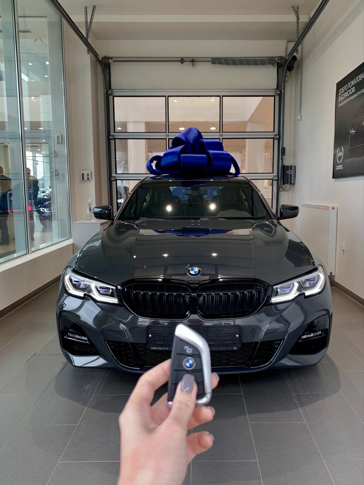 a person holding a cell phone in front of a black car with a blue bow on top