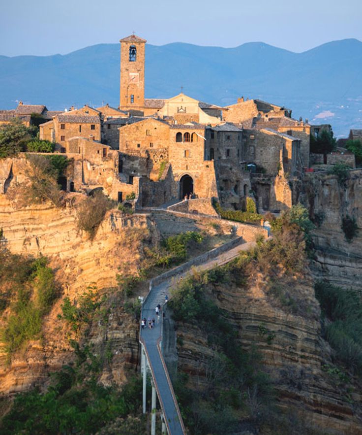 an old village on top of a mountain with a bridge going up the hill to it