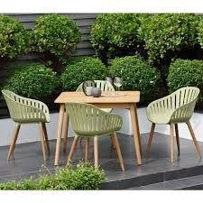 three chairs and a table in front of some bushes on the side of a building