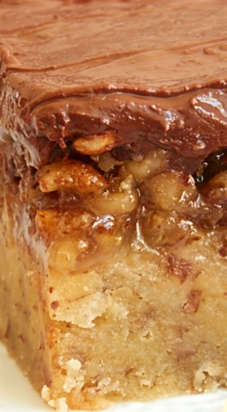 a close up of a piece of cake on a plate with chocolate frosting and nuts