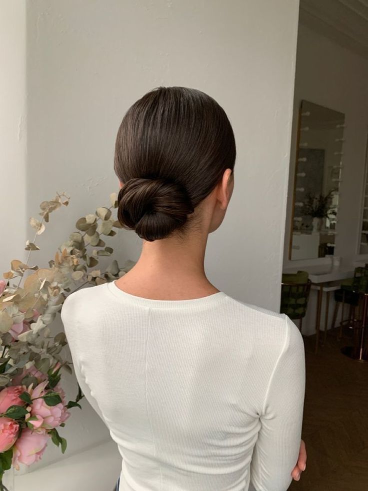 a woman with her back to the camera and flowers behind her, in front of a white wall