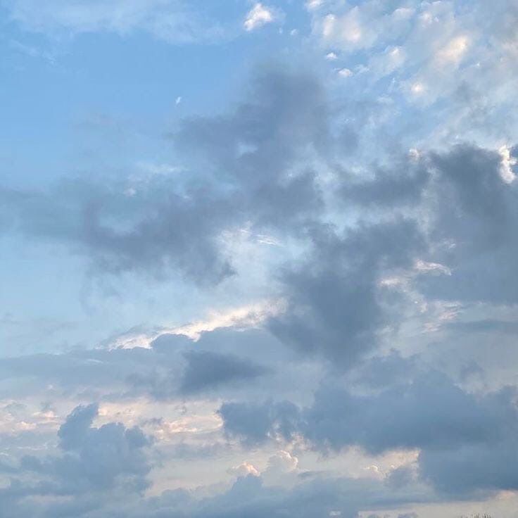 the airplane is flying high in the sky with some clouds above it and trees below