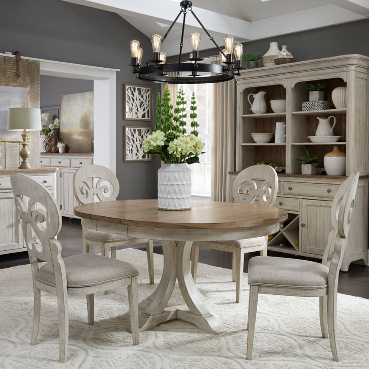 a dining room table with four chairs and a vase on top of it in front of a china cabinet