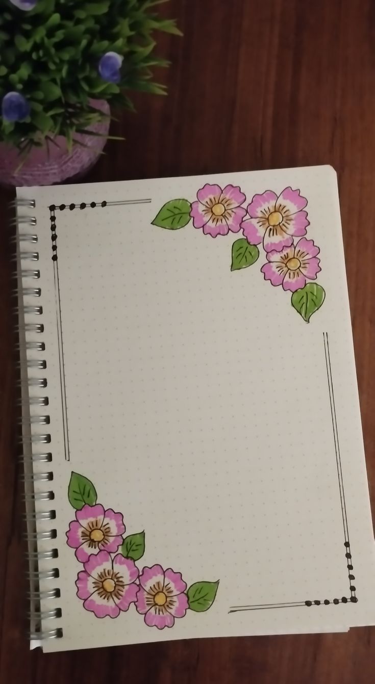 a notebook with flowers painted on it sitting next to a vase filled with purple flowers