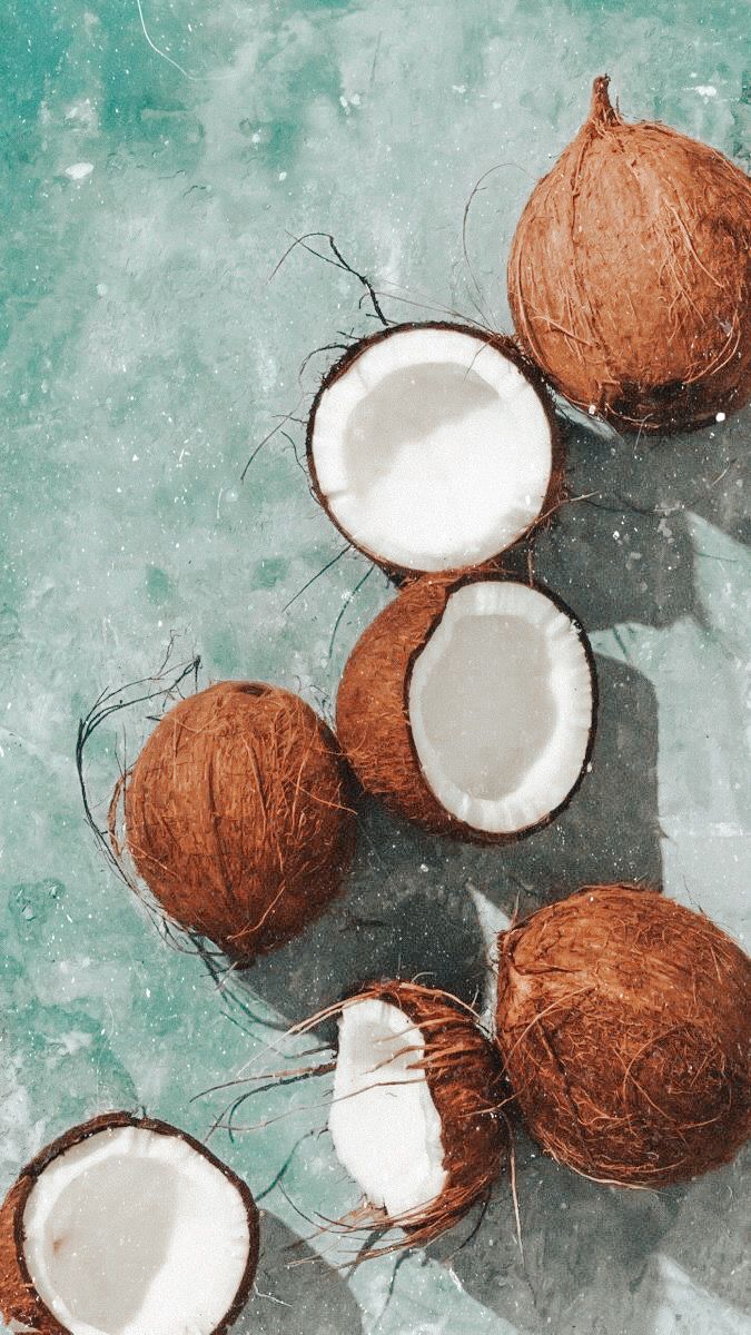 three coconuts with one cut in half and the other whole on a blue surface