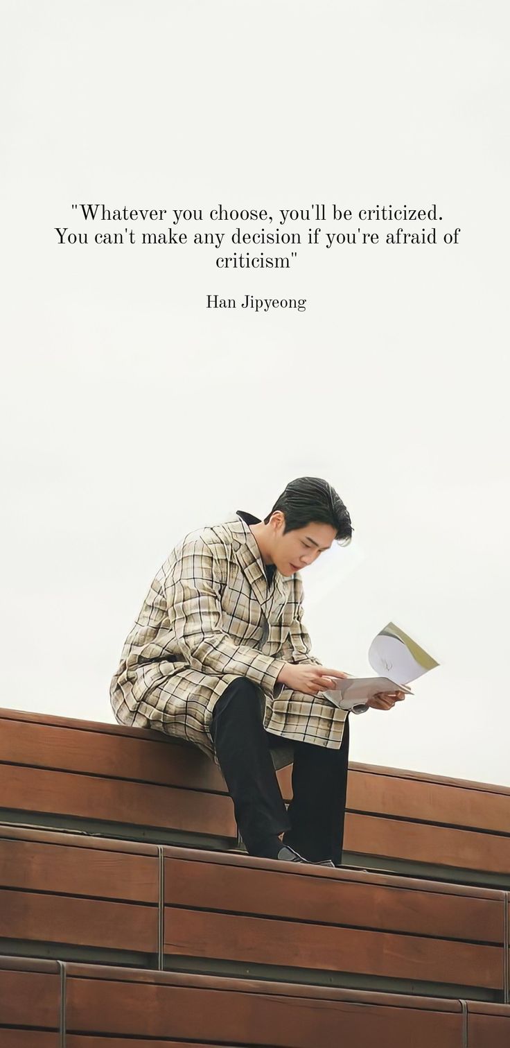 a man sitting on top of a wooden bench next to a wall with a book