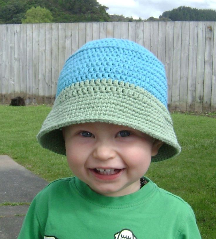 a young boy wearing a crocheted hat in front of a fenced yard