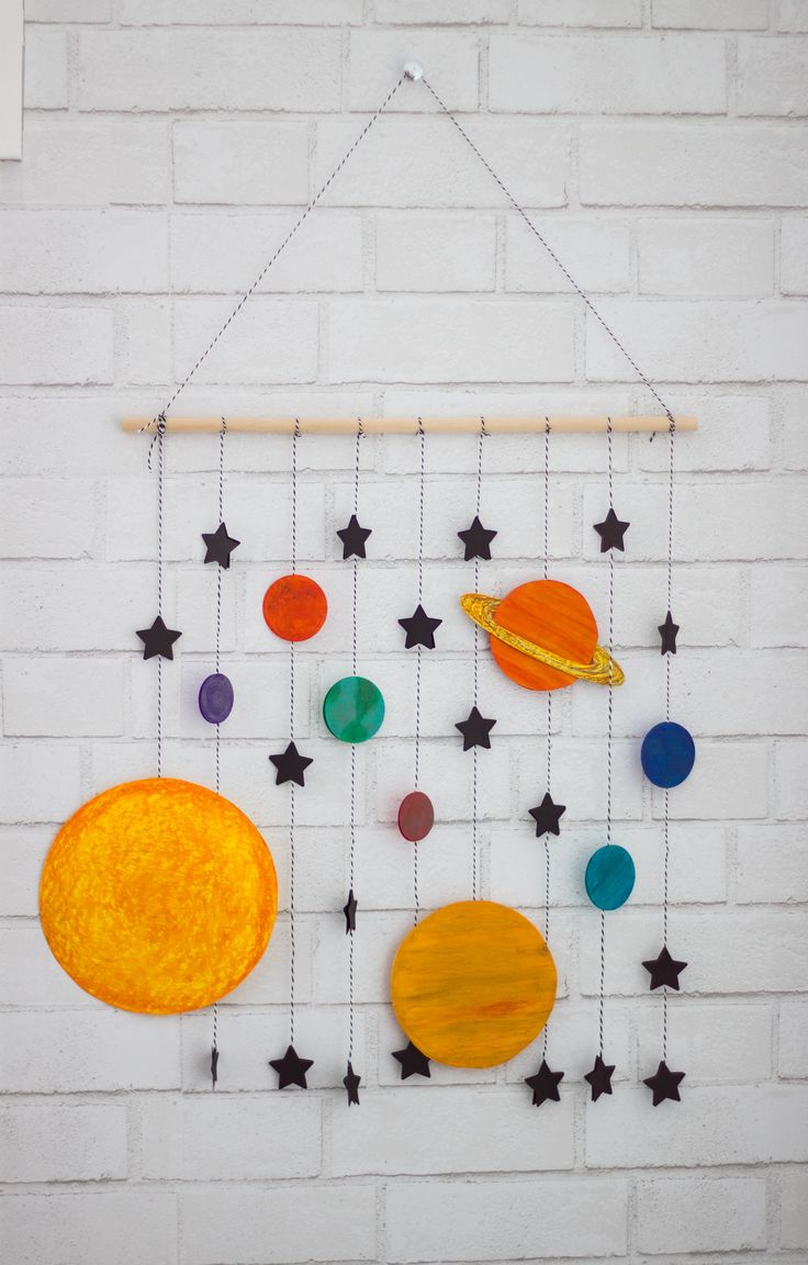 an art project made out of paper and string with planets hanging from the strings on a white brick wall