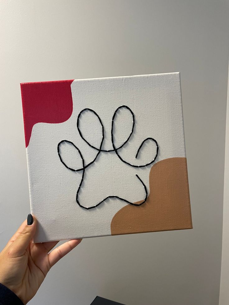 a hand holding up a piece of art with a dog paw on it's side