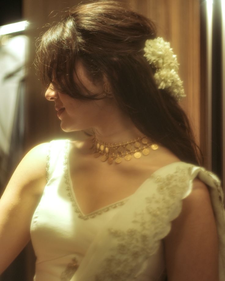 a woman in a white dress with a flower in her hair looking down at something