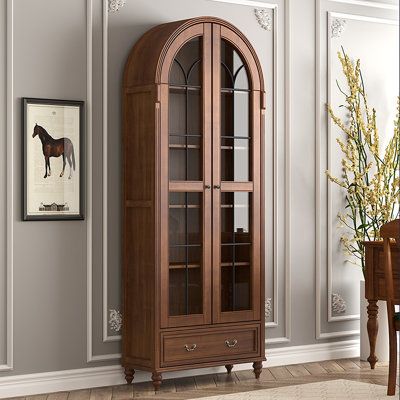 a tall wooden china cabinet sitting in a living room next to a wall with pictures on it